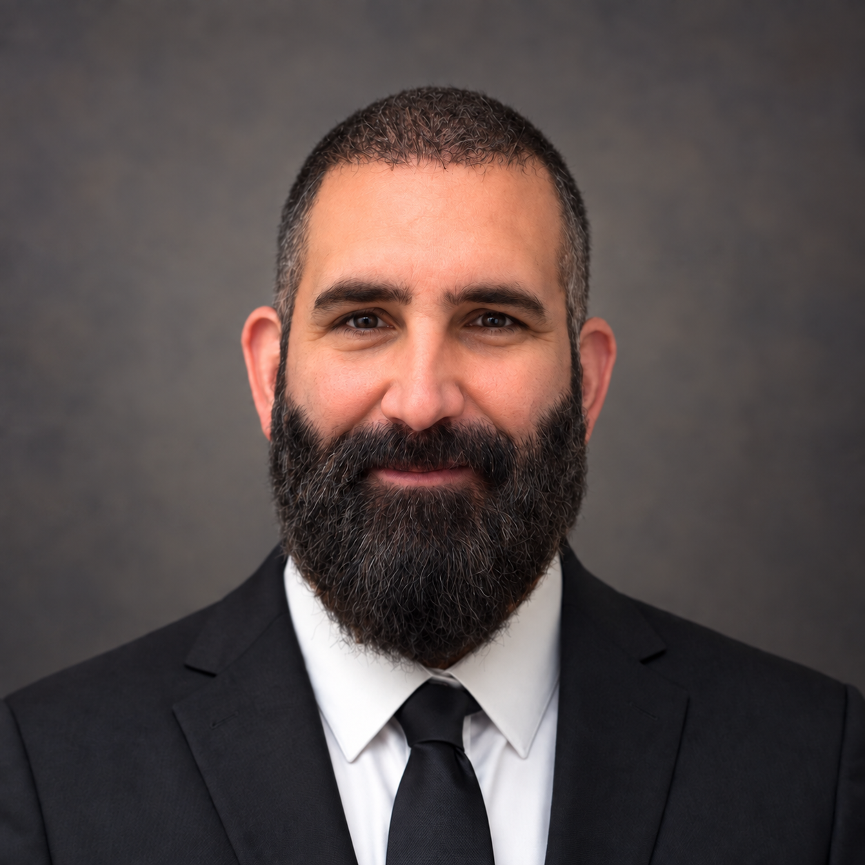 Brian Gillooly, founder and editor-in-chief of Witness Corner, wearing a dark suit and tie against a neutral gray background.